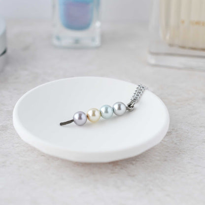 Faux pearl stacked pendant necklace lying in trinket dish on dressing table.