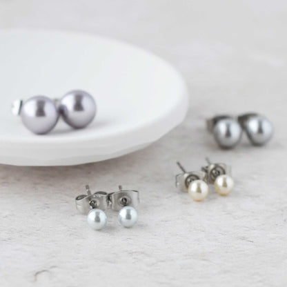 Four pairs of faux pearl stud earrings next to white trinket dish.