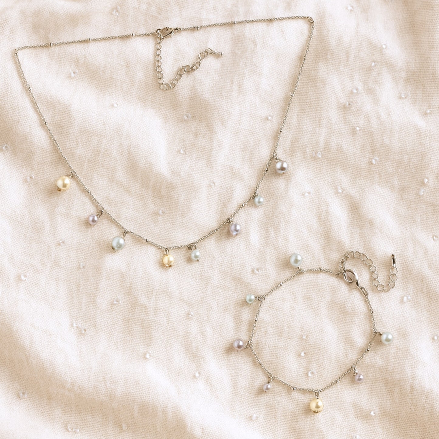 Pearl charms bracelet and necklace on a beige fabric background.