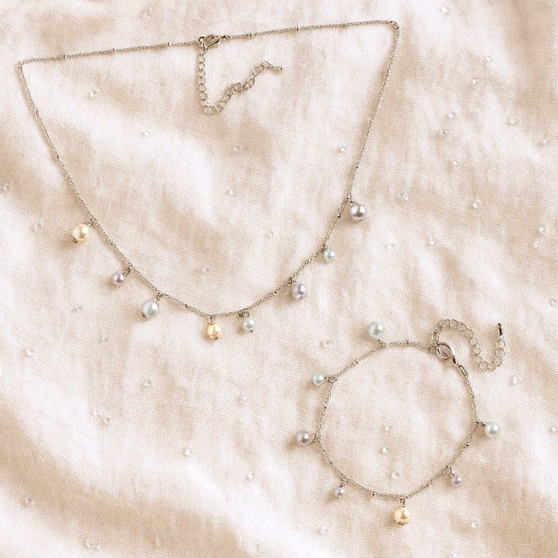 Pearl charms bracelet and necklace on a beige fabric background.
