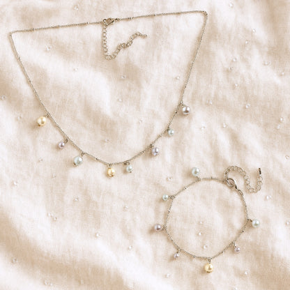 Pearl charms bracelet and necklace on a beige fabric background.