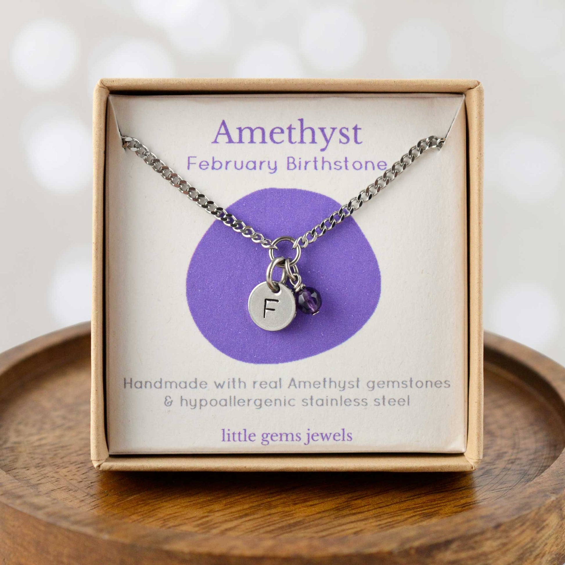 Amethyst February Birthstone necklace with hand stamped initial inside an eco-friendly gift box sitting on wooden coaster