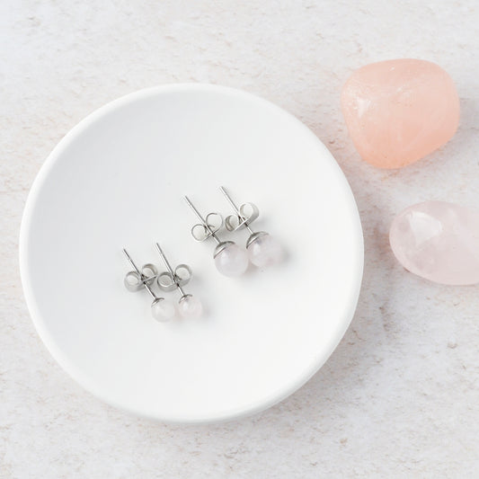Two pairs of Rose Quartz stud earrings on a white trinket dish with pink stones on a light gray background