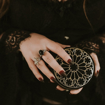 Hand holding a round, intricately designed box with detailed patterns.