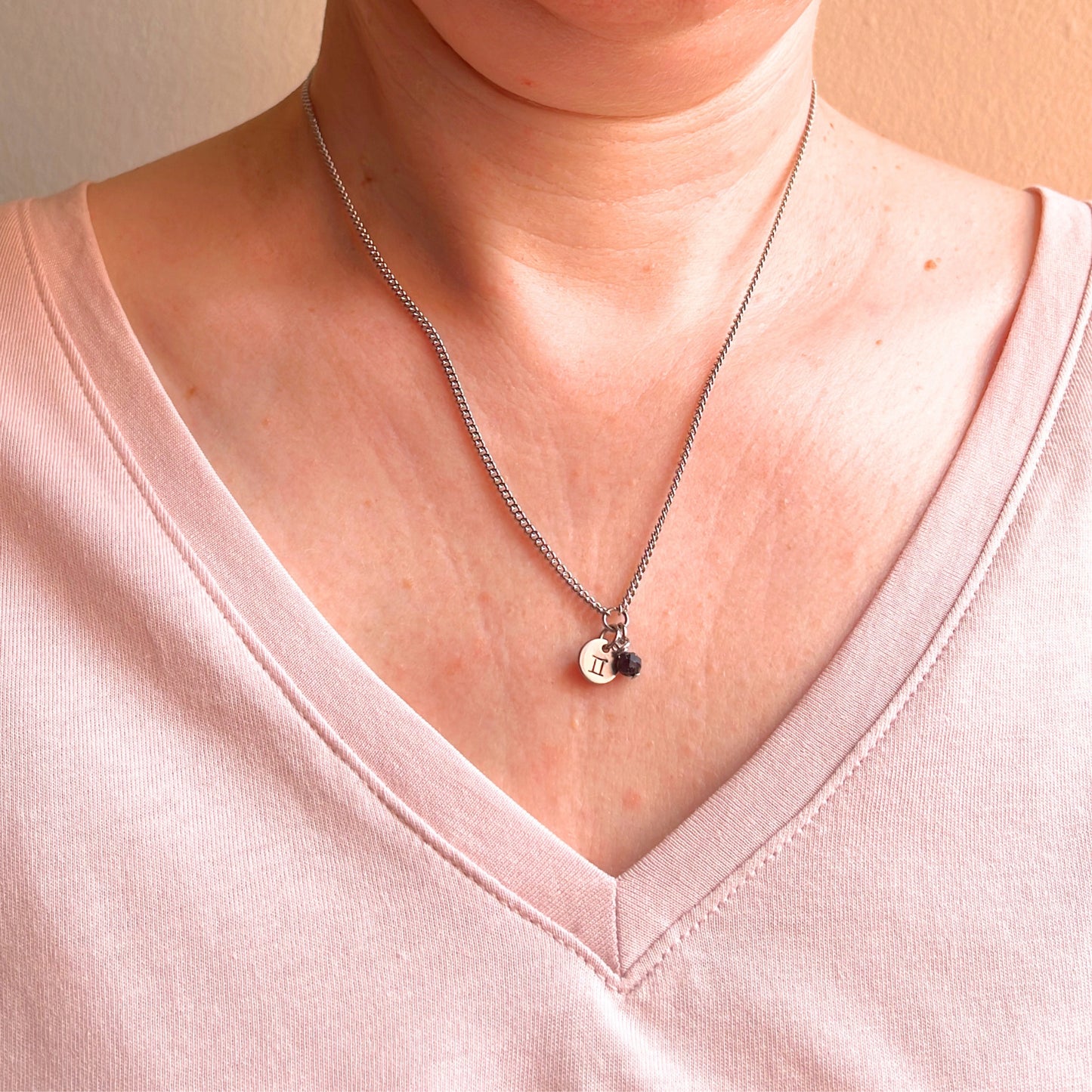 Woman wearing a pink v neck top and dainty Gemini zodiac sign necklace.