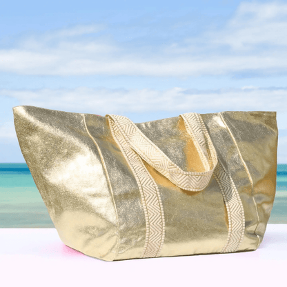 Gold beach bag with textured handle against a blurred beach background