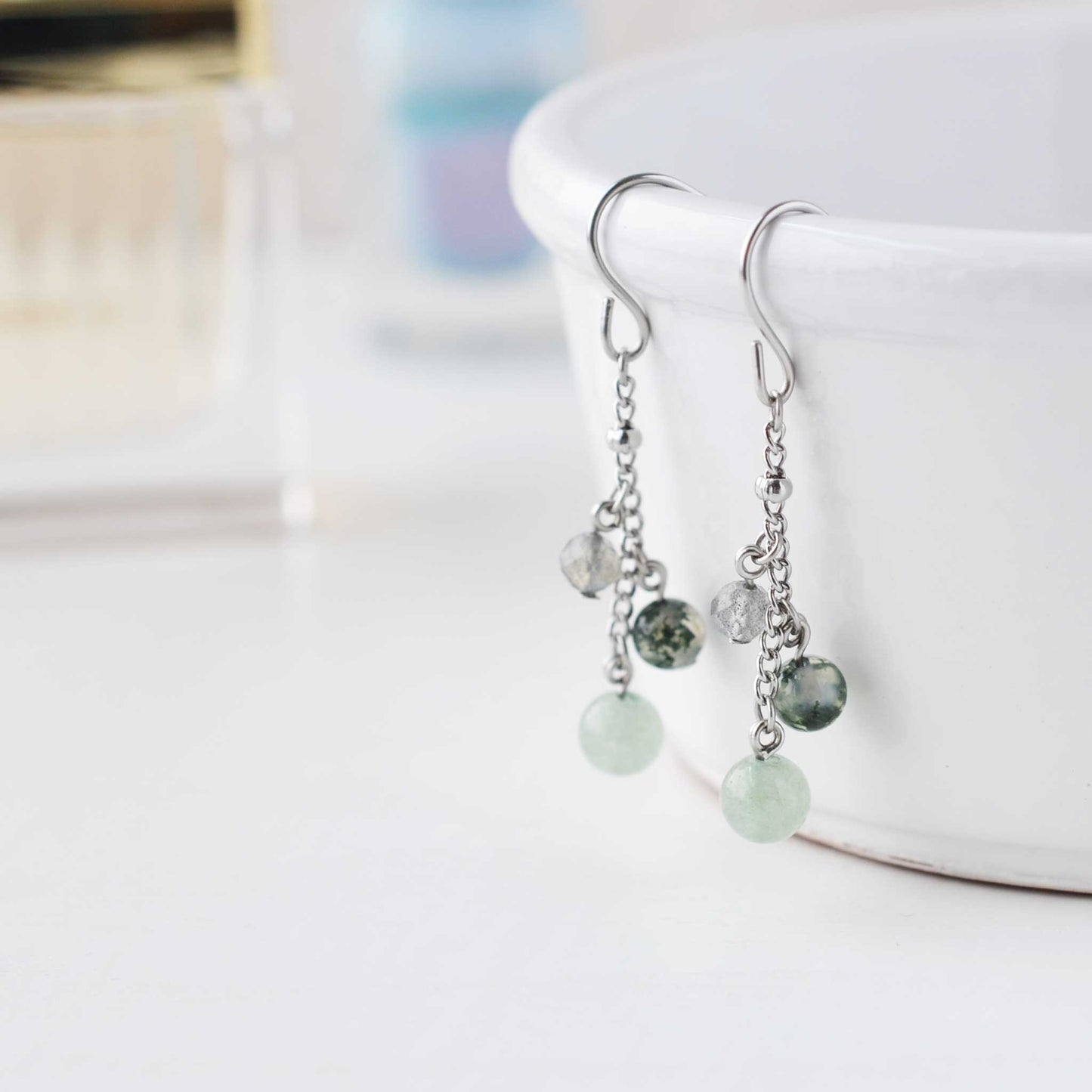 Green gemstone drop earrings hanging froma white cup against soft focus background