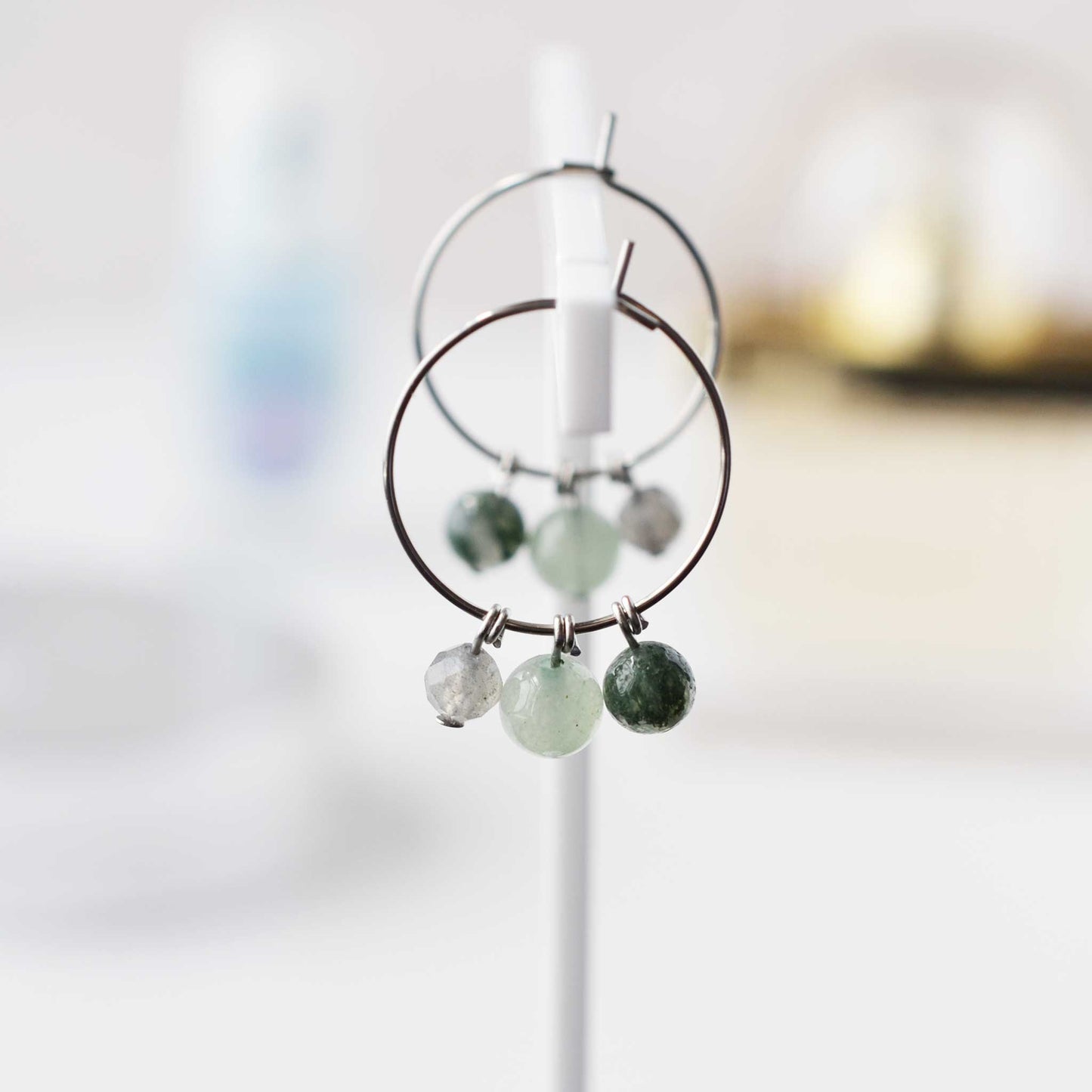 Green gemstone hoop earrings hanging on soft focus background