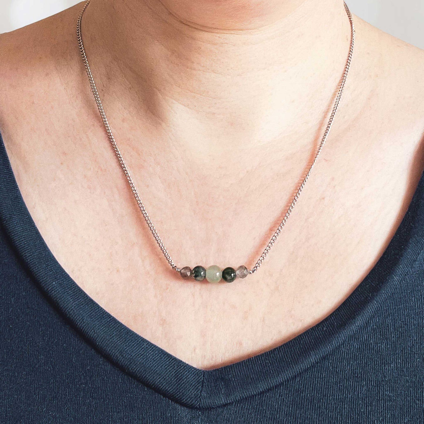 Woman wearing dark blue v neck top and dainty green gemstone necklace