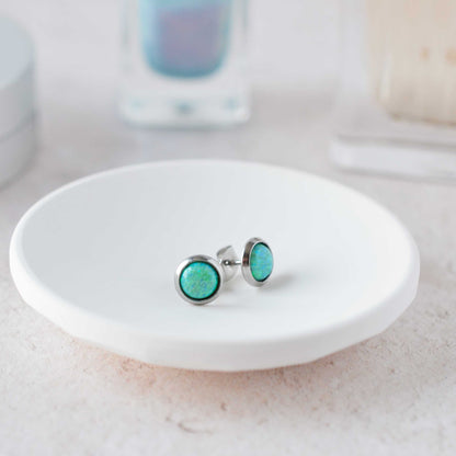 Green stud earrings on a white dish with a blurred background