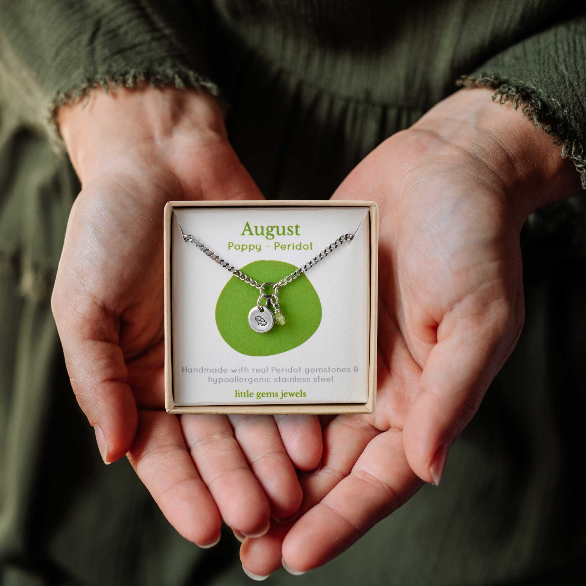 Woman's hands holding a small square eco-friendly gift box containing a dainty August birthflower with Peridot birthstone necklace