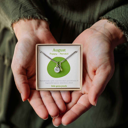 Woman's hands holding a small square eco-friendly gift box containing a dainty August birthflower with Peridot birthstone necklace