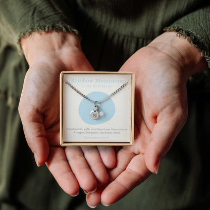 Hands holding a small square eco-friendly gift box containing a tiny initial and June Moonstone birthstone necklace