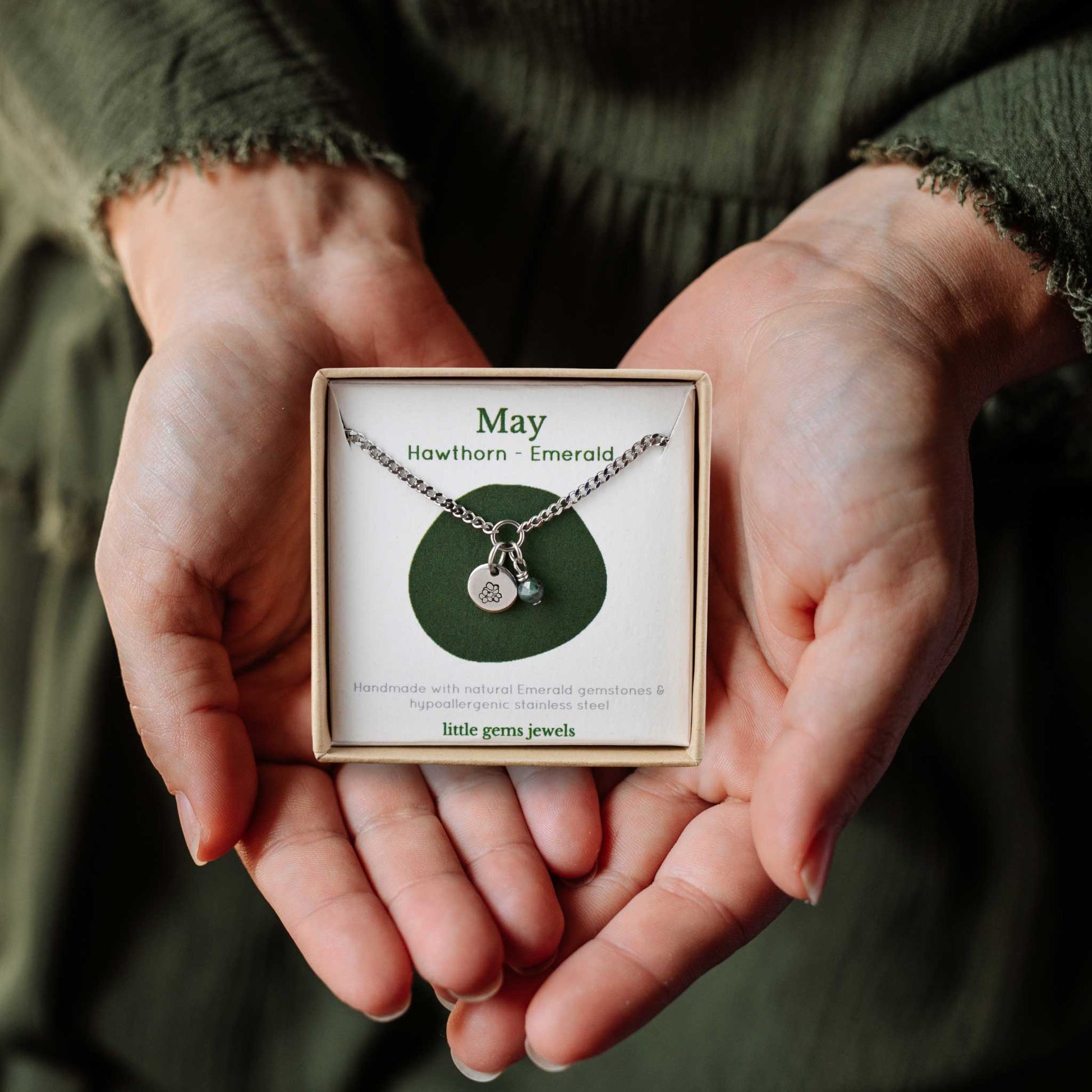 Woman's hands holding a small square eco-friendly gift box containing a dainty May birthflower with Emerald birthstone necklace