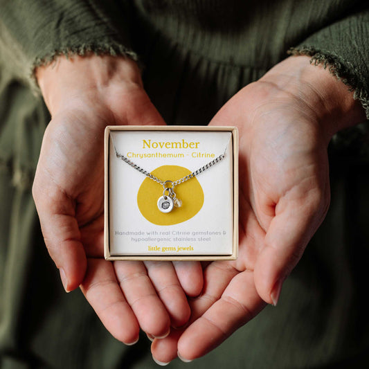 Woman's hands holding a small square eco-friendly gift box containing a dainty November birthflower with Citrine birthstone necklace