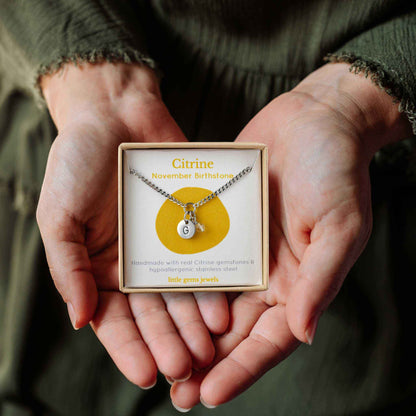 Hands holding a small square eco-friendly gift box containing a tiny initial and Citrine November birthstone necklace