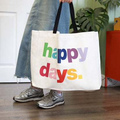 Person holding a white tote bag with 'happy days' text in colorful letters.