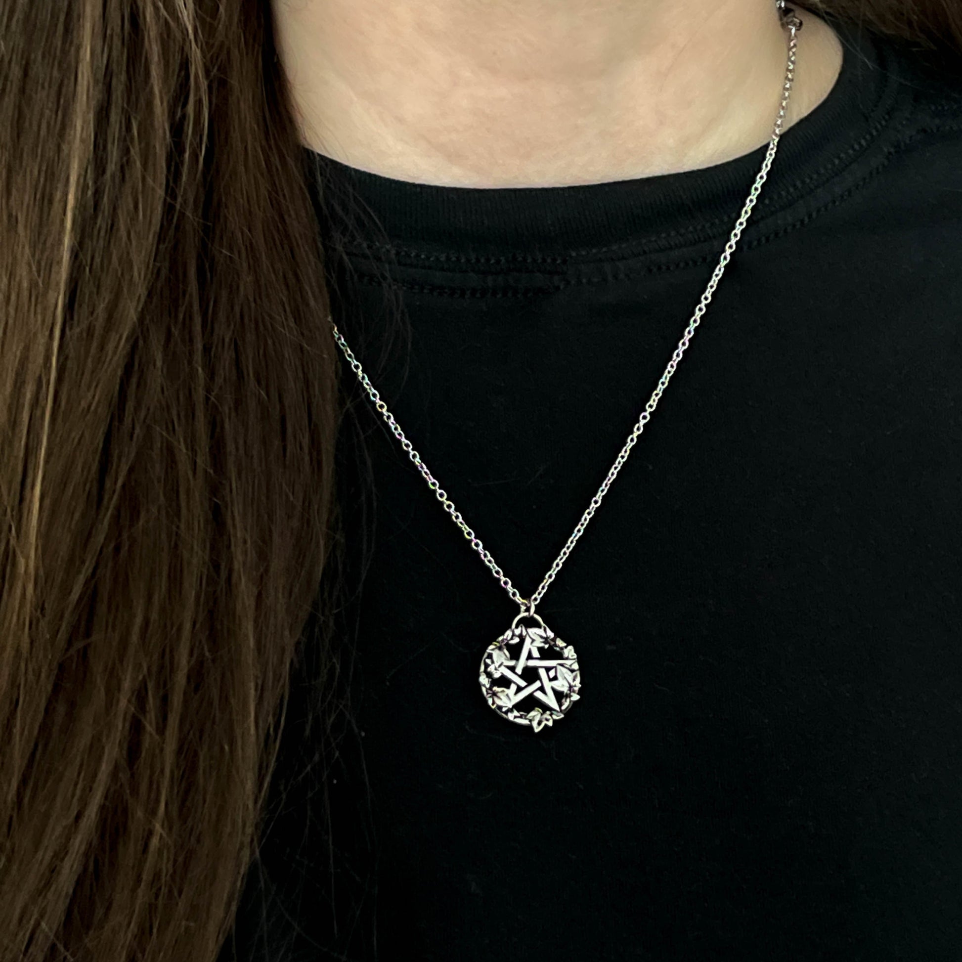 Person wearing a steel necklace with a star pendant on a black background