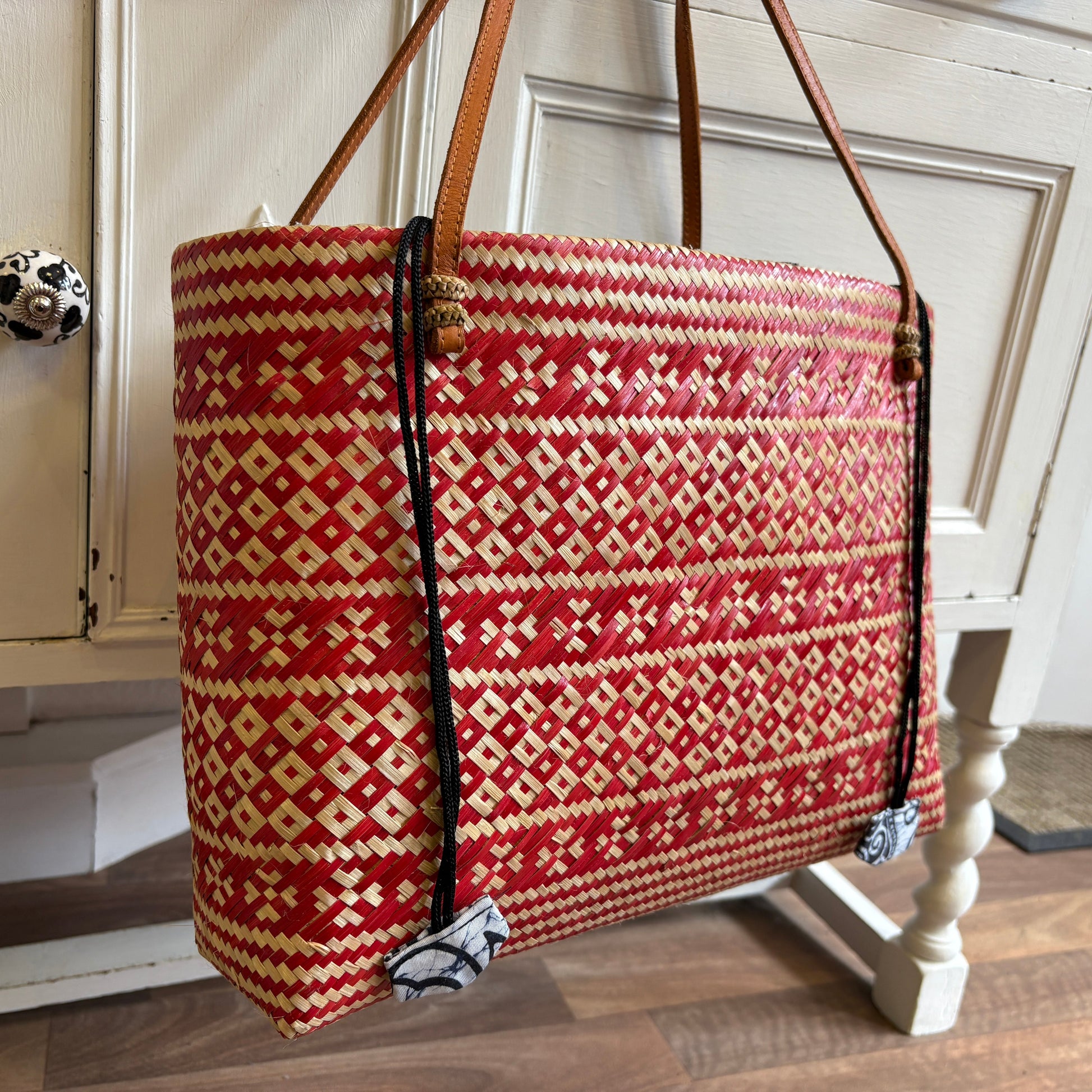 Red and beige patterned bag with brown handles on a wooden floor.