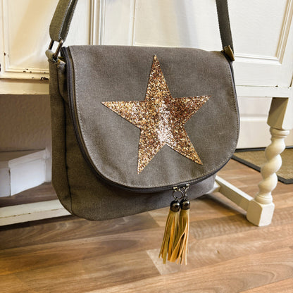 Gray shoulder bag with a gold star and tassels on a wooden floor.
