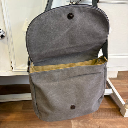 Gray backpack with open front pocket on a wooden floor.