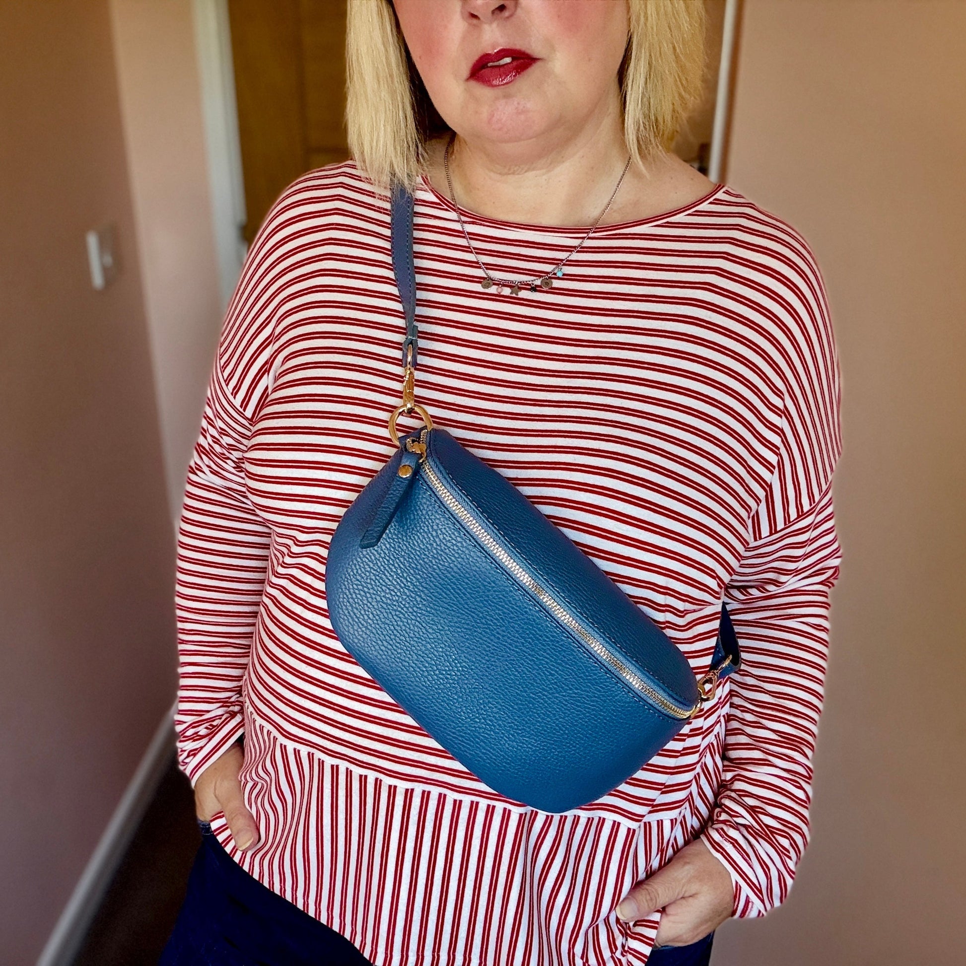 Woman wearing a red and white striped shirt with a blue bag, standing against a plain wall.