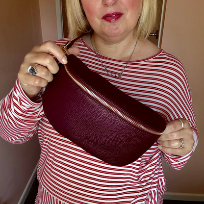 Woman holding a burgundy leather bag with gold zipper against a neutral background