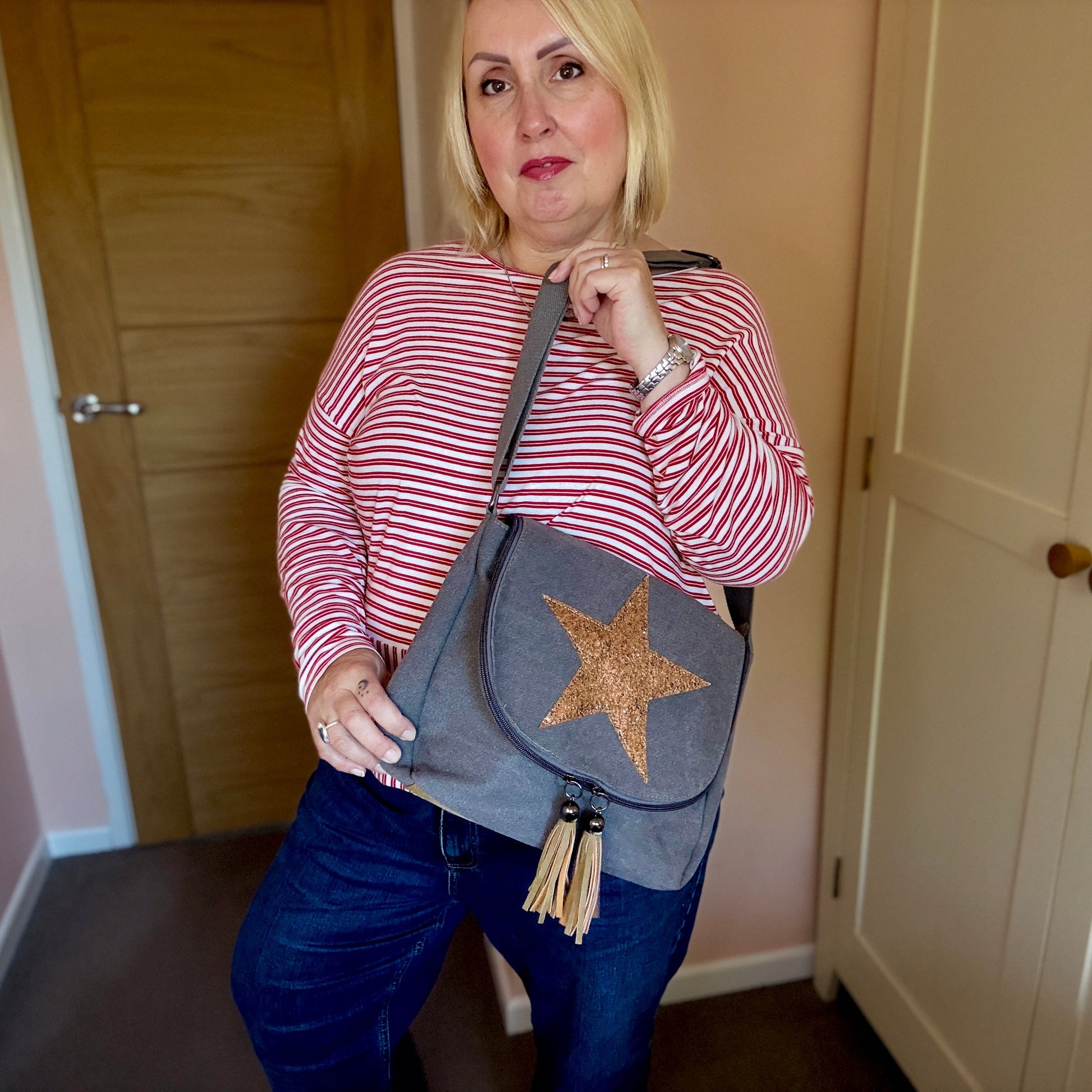 Woman holding a gray crossbody bag with a star design in a room.