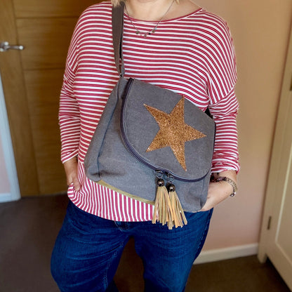 Woman wearing a striped shirt and blue jeans, holding a gray bag with a star design.