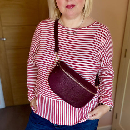 Woman wearing a red and white striped shirt and blue jeans, holding a maroon handbag indoors.
