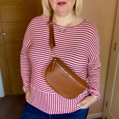 Woman wearing a red and white striped shirt and blue jeans, holding a brown handbag indoors.