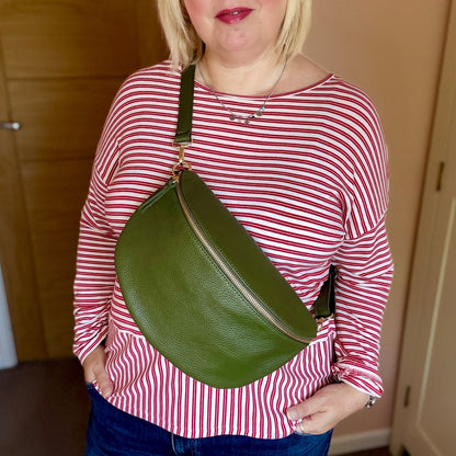 Woman holding a green bag indoors against a neutral background