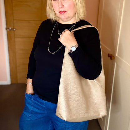 Woman holding a gold handbag indoors with a neutral background