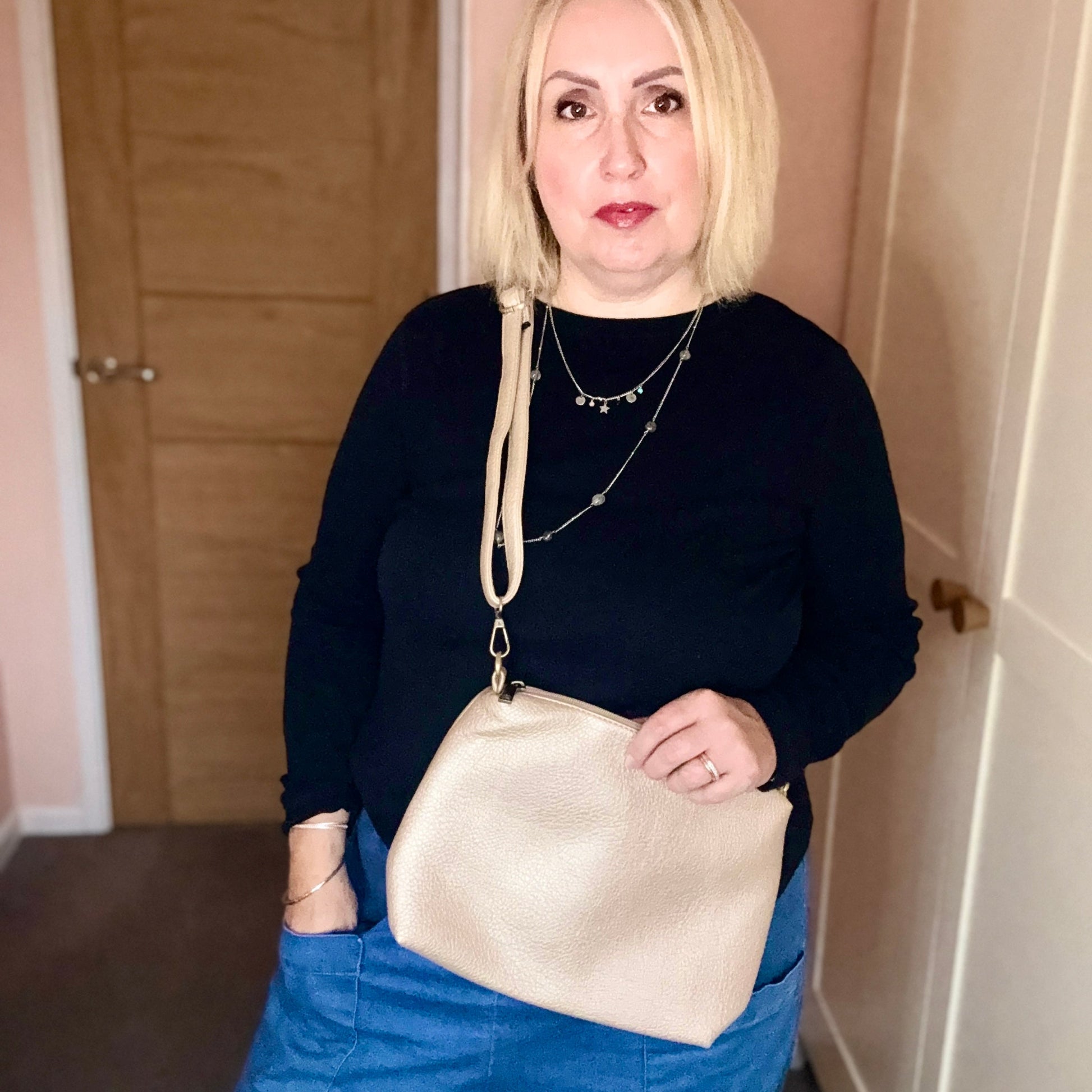 Woman holding a gold handbag indoors against a neutral background