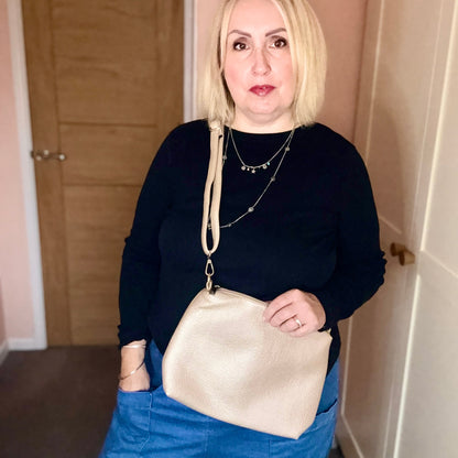 Woman holding a gold handbag indoors against a neutral background