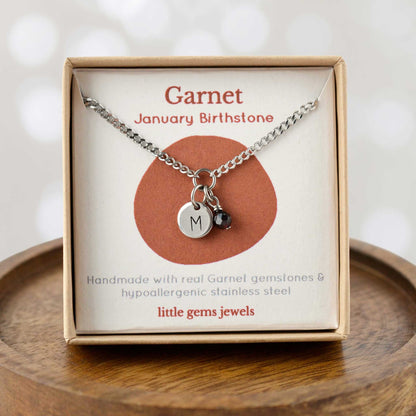 Garnet January Birthstone necklace with hand stamped initial inside an eco-friendly gift box sitting on wooden coaster