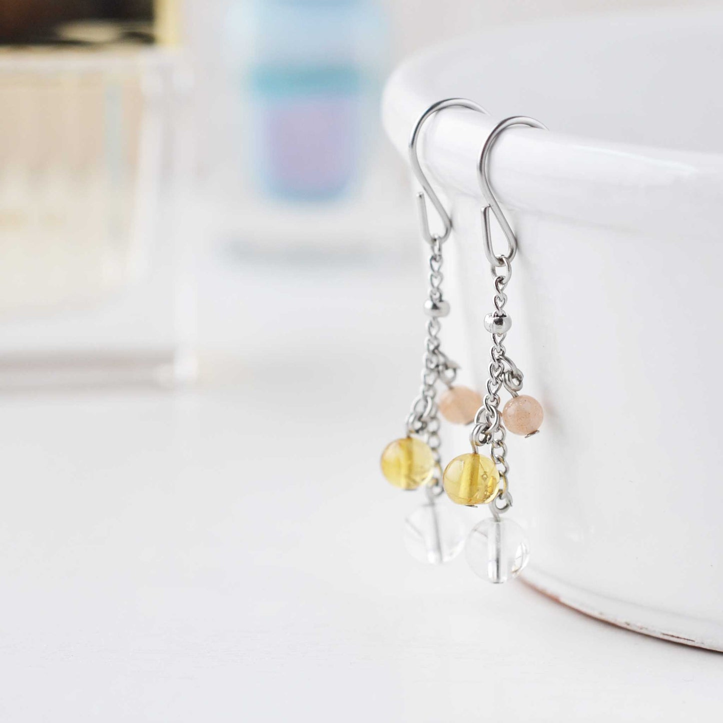 Yellow gemstone drop earrings hanging from white dish against soft focud background