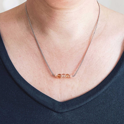 Woman wearing dark blue v neck top and dainty yellow gemstone necklace