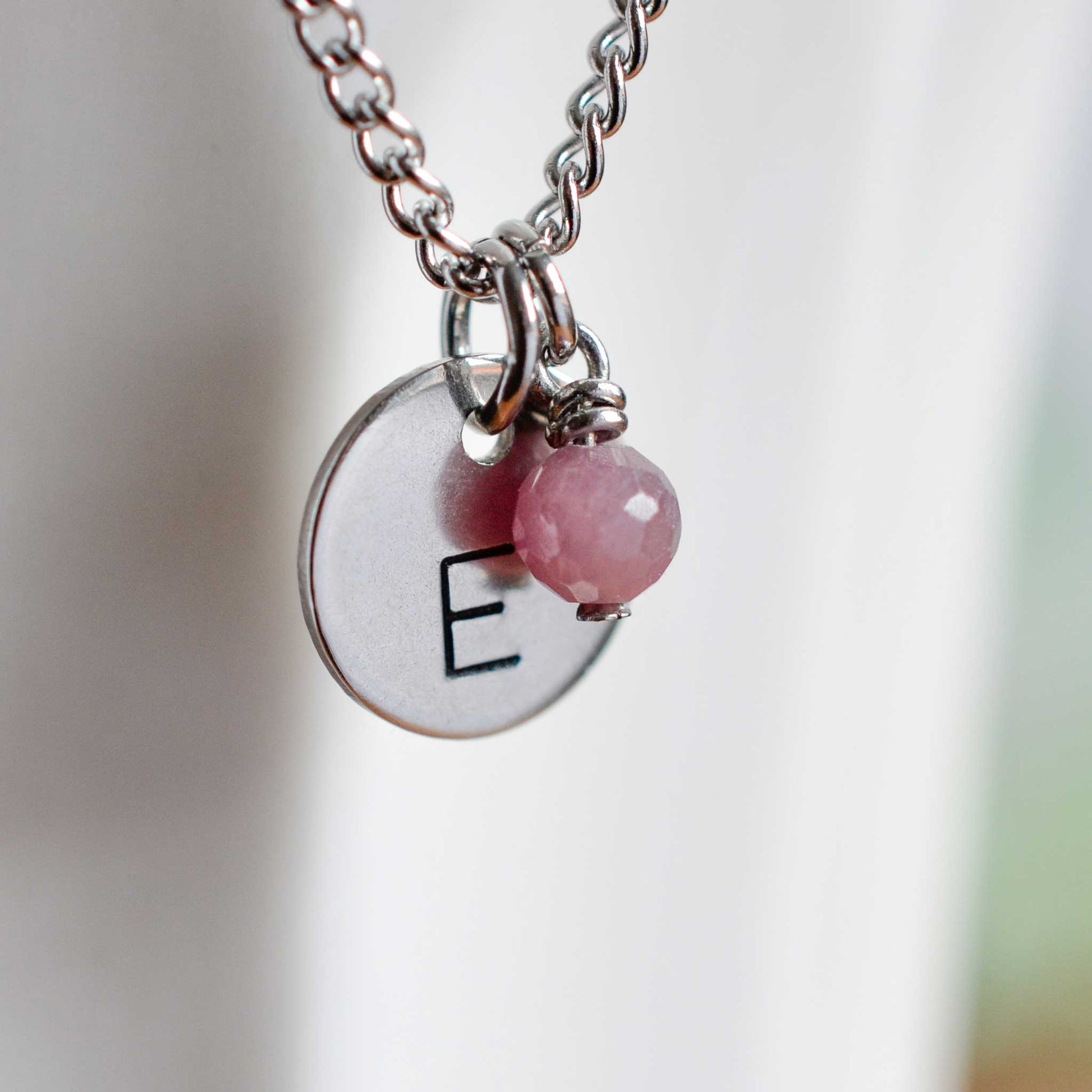 Close up of letter E disc initial pendant with Ruby July birthstone charm