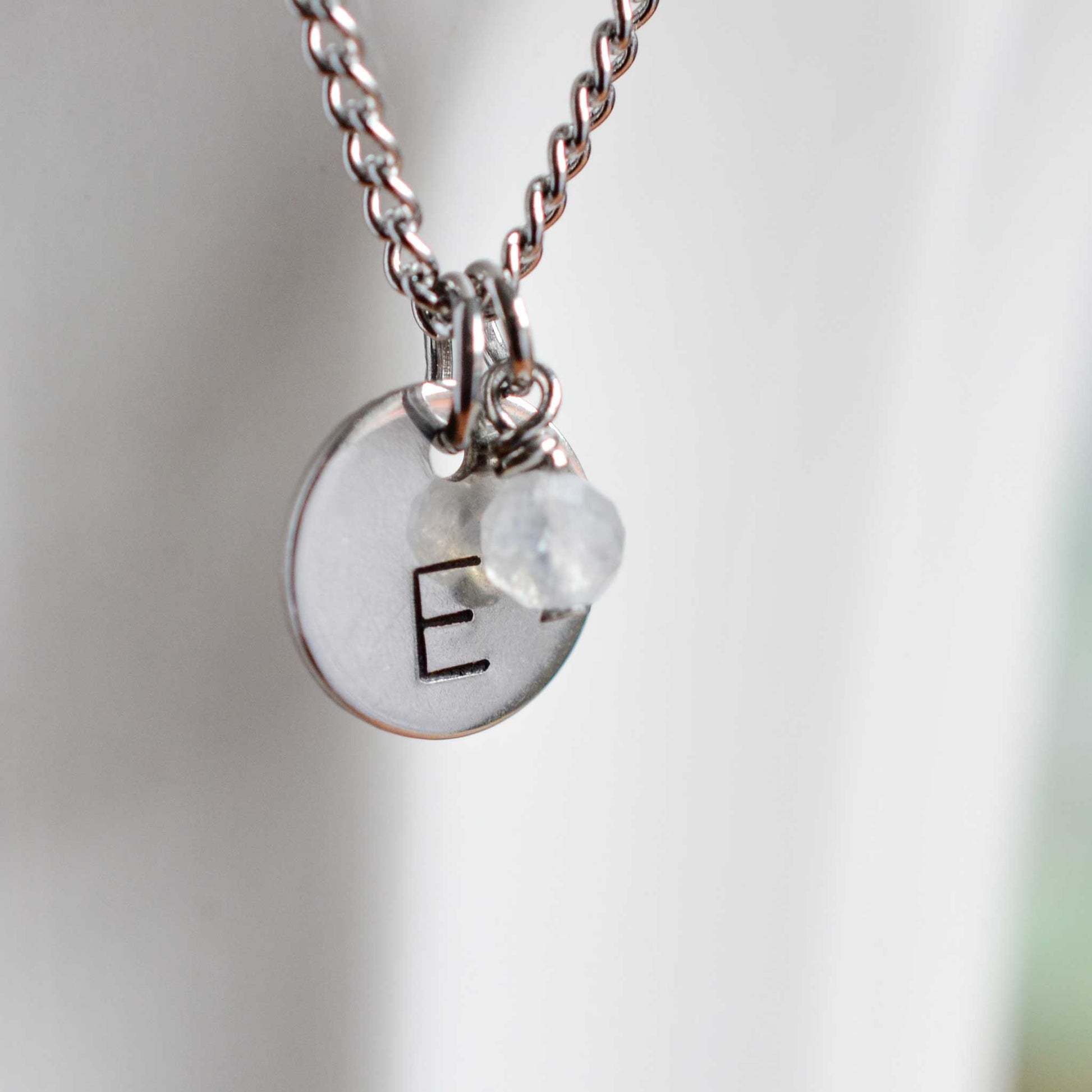 Close up of letter E disc initial pendant with Moonstone June birthstone charm