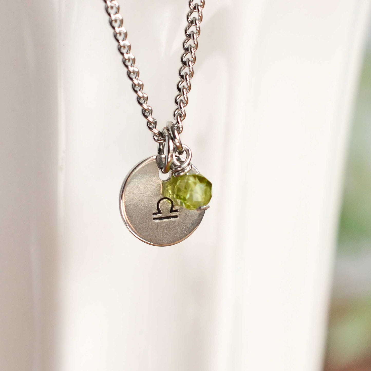 Close up of Libra zodiac sign necklace with Peridot gemstone charm on stainless steel chain