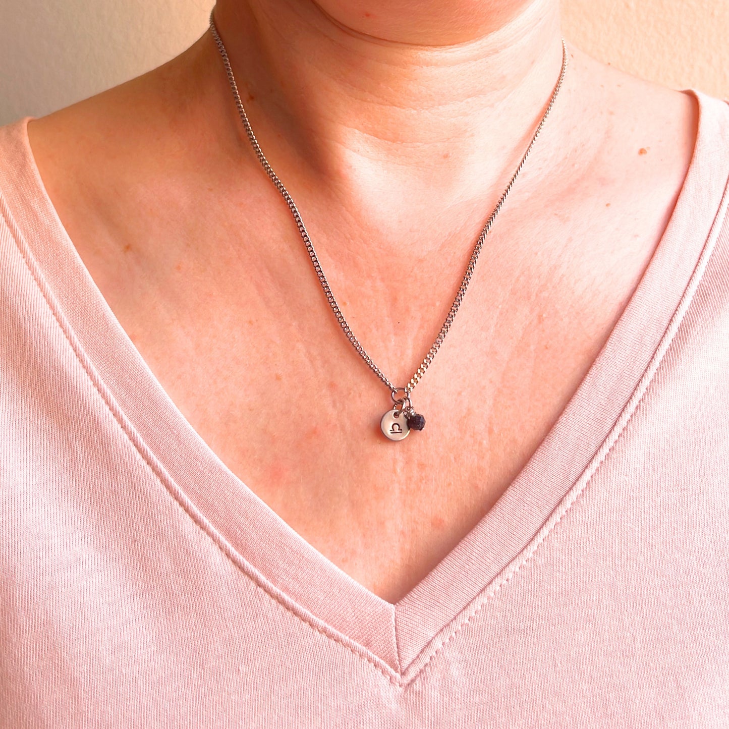 Woman wearing a pink v neck top and dainty Libra zodiac sign necklace.