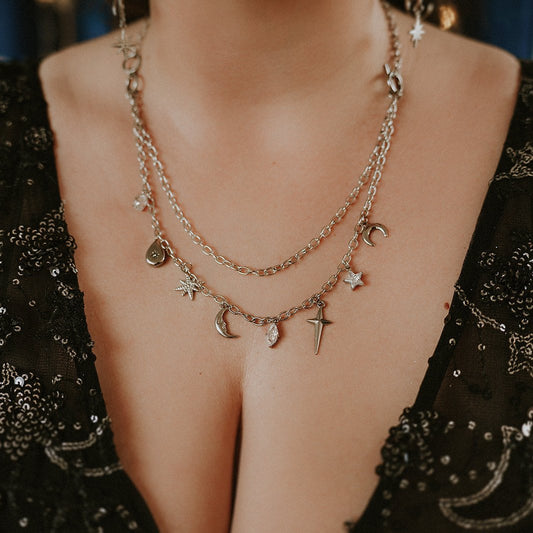 Layered stainless steel necklaces with charms on a person wearing a black embellished outfit.