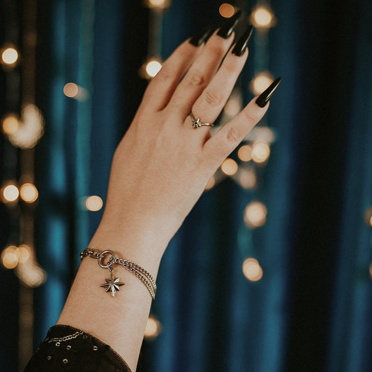 Hand with black nail polish wearing a ring and bracelet against a blurred light background