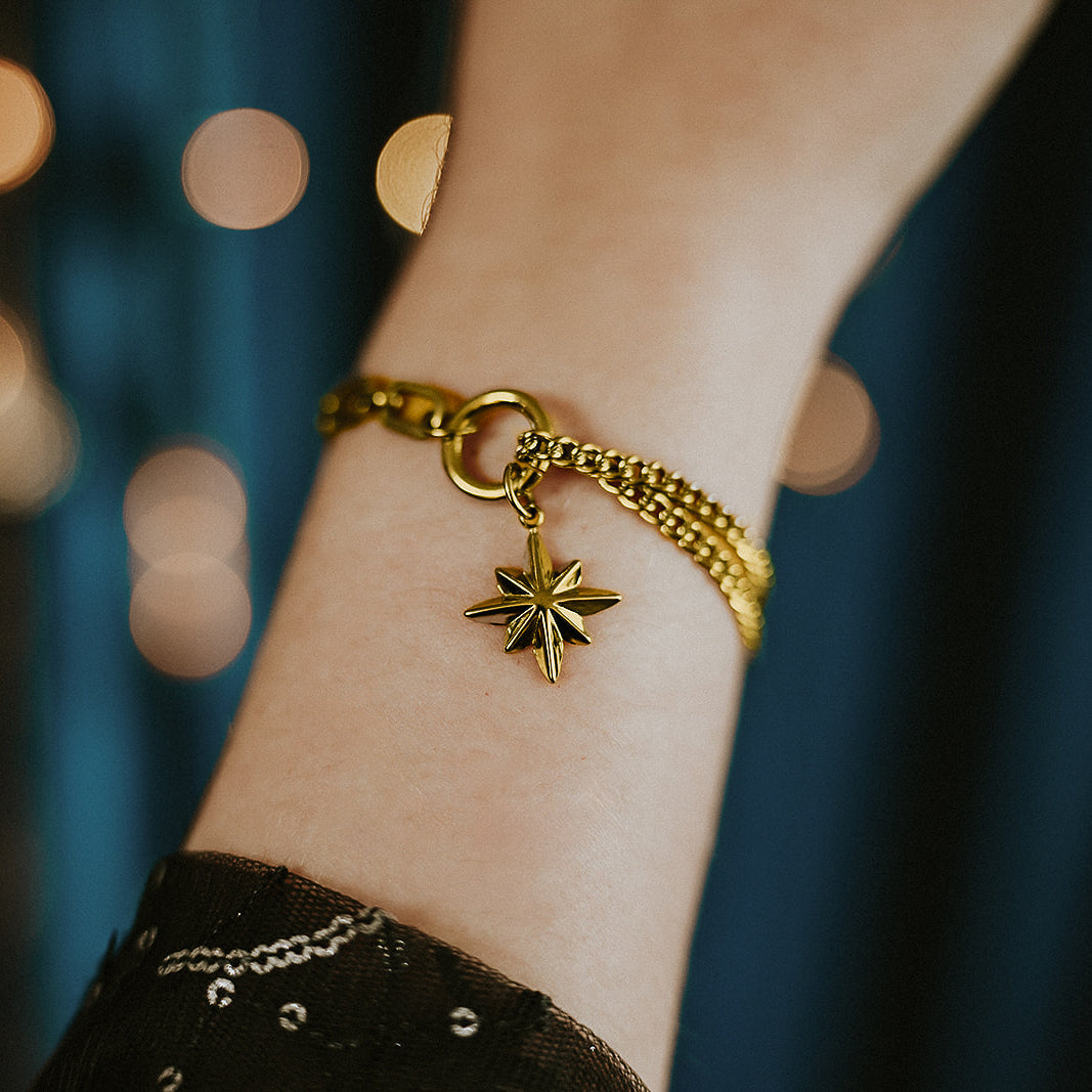 Gold bracelet with a star charm on a wrist against a blurred background