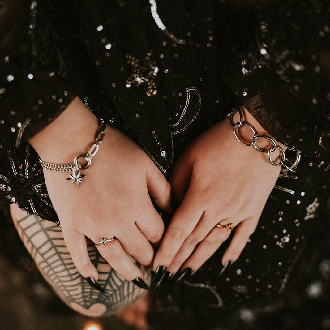 Close-up of hands wearing steel bracelets and rings against a dark, textured background.