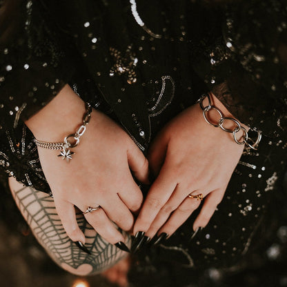 Close-up of hands wearing steel bracelets and rings against a dark, textured background.