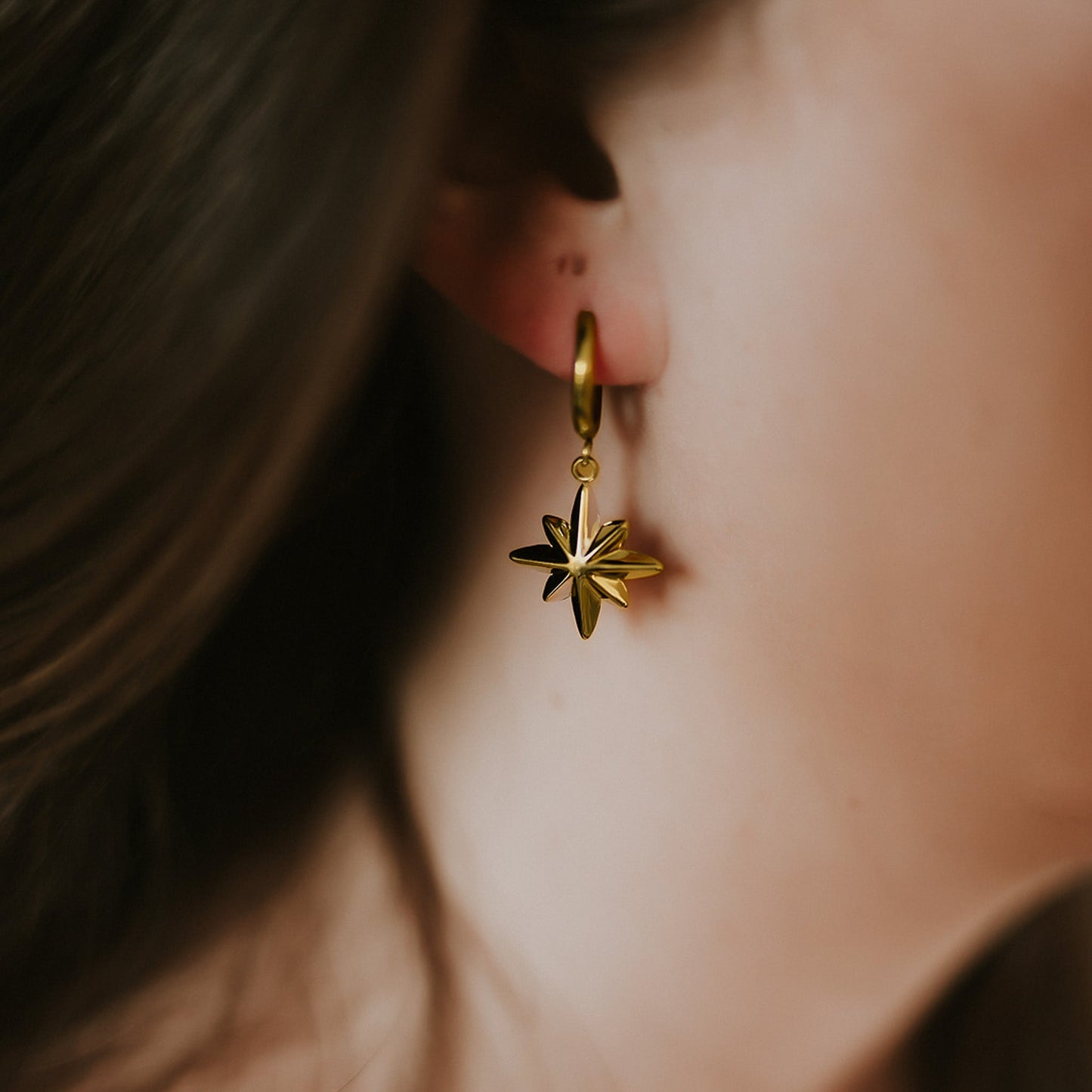 Close-up of a person wearing a gold earring with a star-shaped pendant.