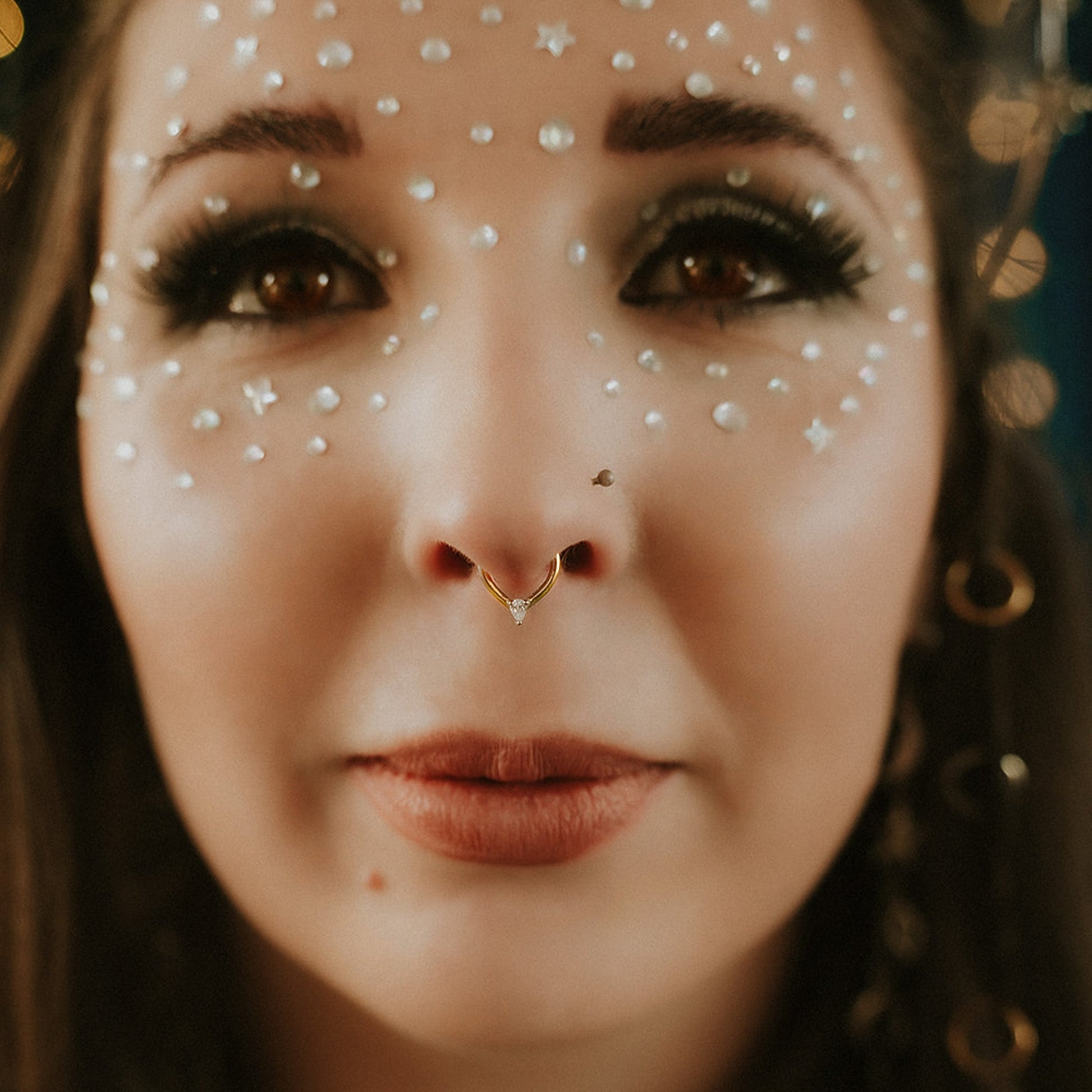 Close-up of a person with decorative face makeup and a gold nose ring.