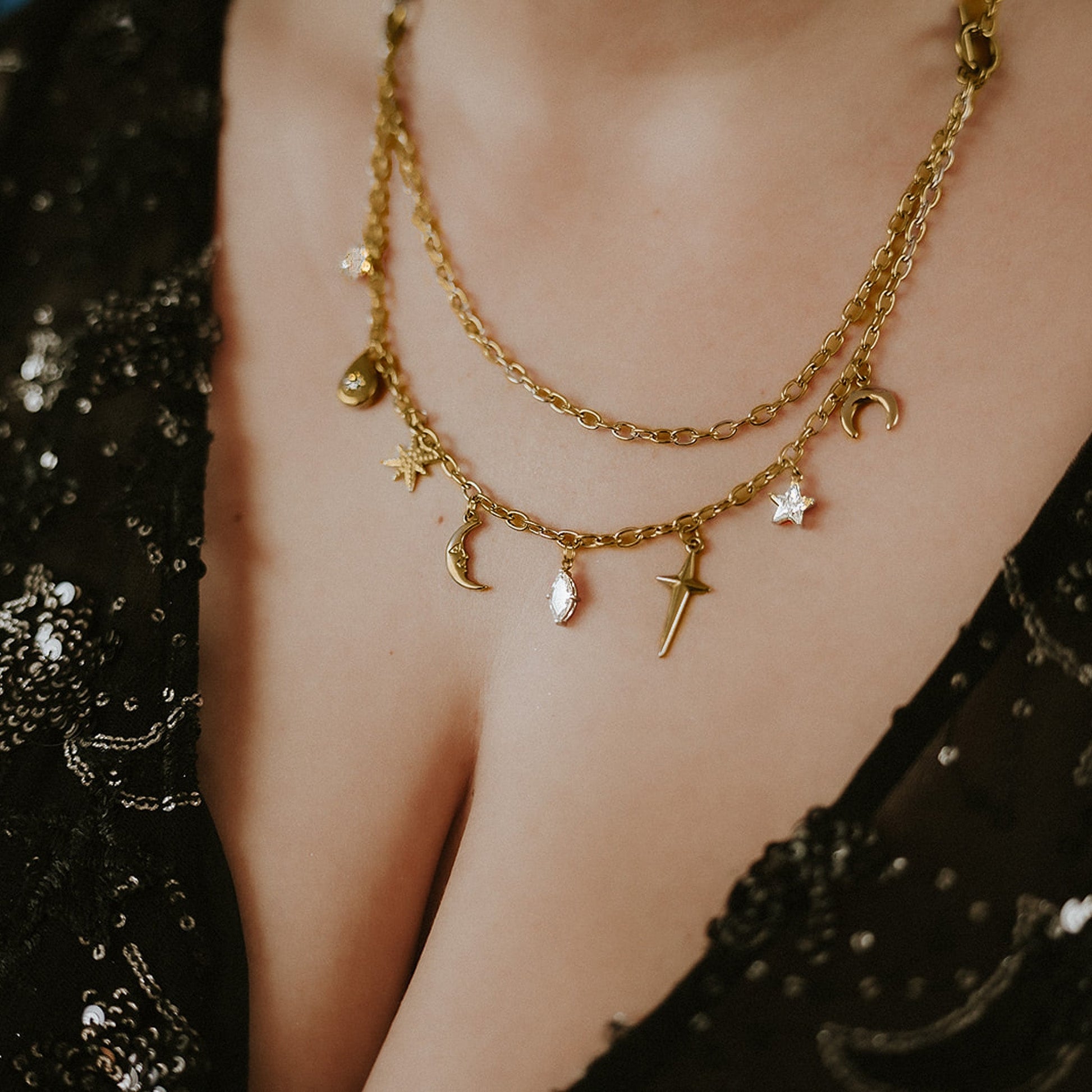 Gold chain necklace with charms worn by a person against a dark background